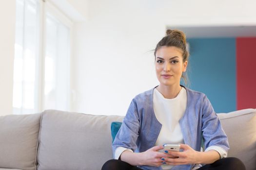 young happy woman using mobile phone on sofa at luxury home