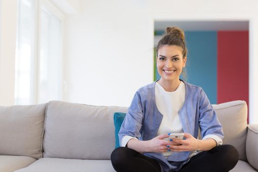 young happy woman using mobile phone on sofa at luxury home