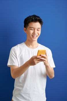 Smiling young good looking Asian man using smartphone to get in touch with family and friends isolated on blue  background