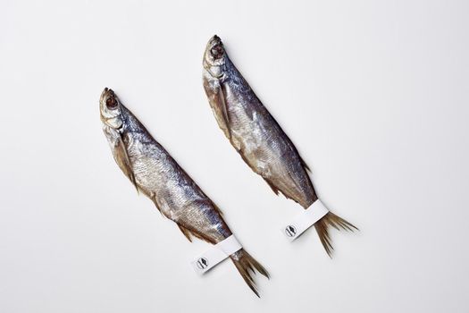 Two salted sun-dried sabrefish with paper labels on tails lying on white background, top view with copyspace