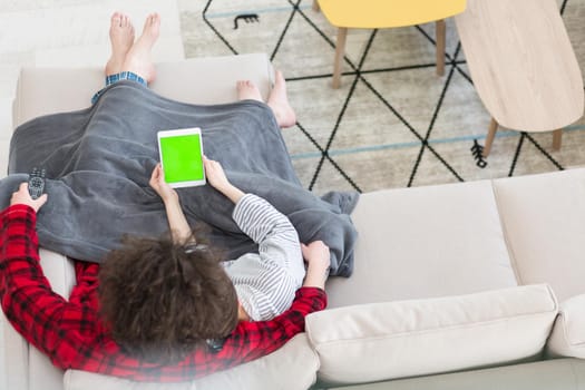 Young couple relaxing at  home using tablet computers reading in the living room on the sofa couch.