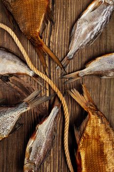 Bunch of tails of salted dried and smoked fish of different sizes lying on rough rustic wooden surface with coarse rope. Artisanal drying of fish