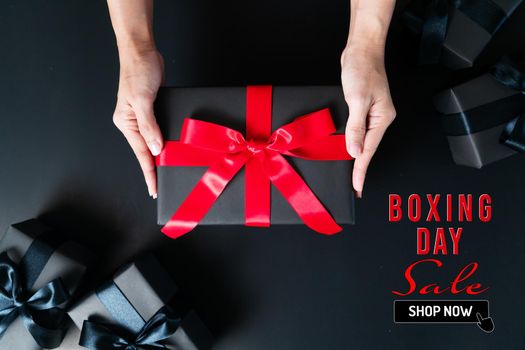 Boxing Day sale, woman hand give the gift box on black background
