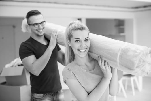 Young couple carrying a carpet moving in to new home together. Home, people, moving and real estate concept