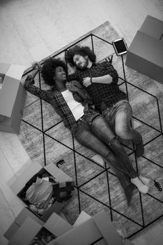 Top view of attractive young multiethnic couple moving, holding hands, looking at camera and smiling while lying among cardboard boxes