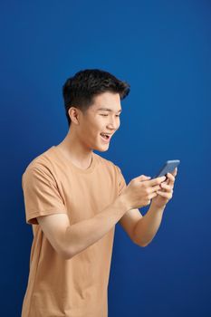 Smiling young good looking Asian man using smartphone to get in touch with family and friends isolated on blue  background