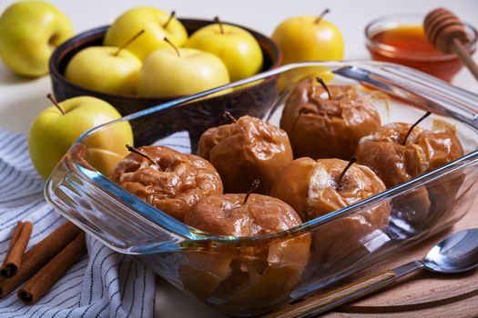 Baked caramelized apples with honey in glass refractory baking dish are placed on table among yellow apples. Selective focus.