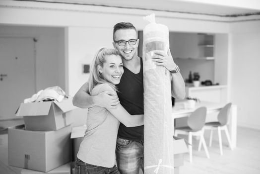 Young couple carrying a carpet moving in to new home together. Home, people, moving and real estate concept