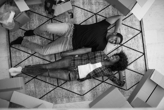 Top view of attractive young African American couple moving, holding hands, looking at camera and smiling while lying among cardboard boxes