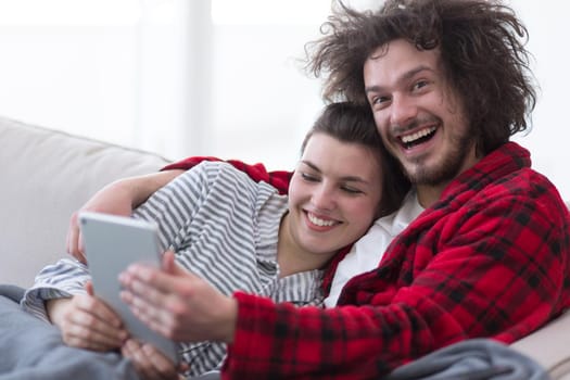 Young couple relaxing at  home using tablet computers reading in the living room on the sofa couch.