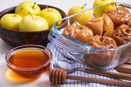 Baked caramelized apples with honey in glass refractory baking dish are placed on table among yellow apples. Selective focus.