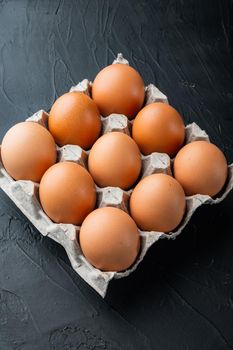 Raw chicken eggs in egg box set, on black background