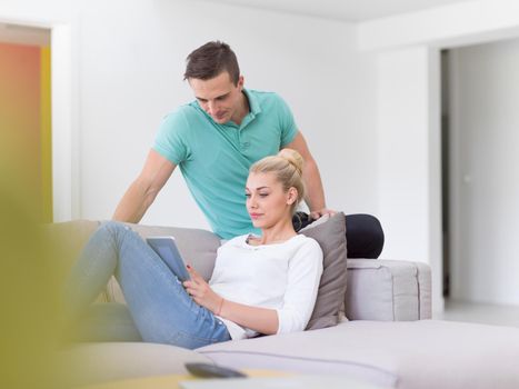 Young couple relaxing at luxurious home with tablet computers reading in the living room on the sofa couch.