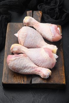 Primal cut of raw chicken legs, with chicken thighs and drumsticks set, on wooden cutting board, on black stone background