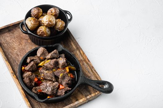 Meat stew with sweet bell pepper and bay leaf set, in cast iron frying pan, on white stone surface, with copy space for text