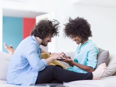 Young multiethnic couple sitting on a sofa in the luxury living room, using a tablet computer