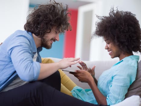 Young multiethnic couple sitting on a sofa in the luxury living room, using a tablet computer