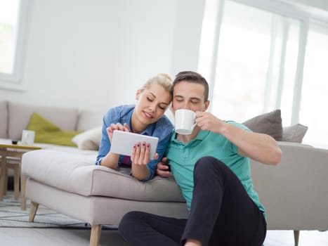 Young couple relaxing at luxurious home with tablet computers reading in the living room on the sofa couch.