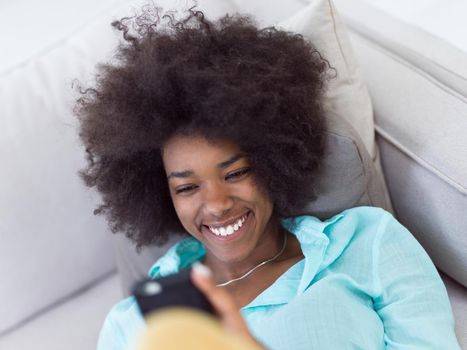 young happy african american woman sitting on sofa and using mobile phone at luxury home