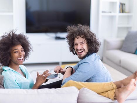 Young multiethnic couple sitting on a sofa in the luxury living room, using a tablet computer