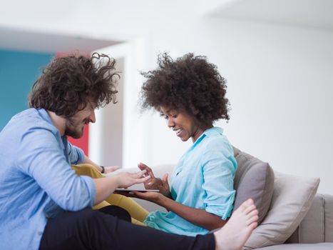 Young multiethnic couple sitting on a sofa in the luxury living room, using a tablet computer