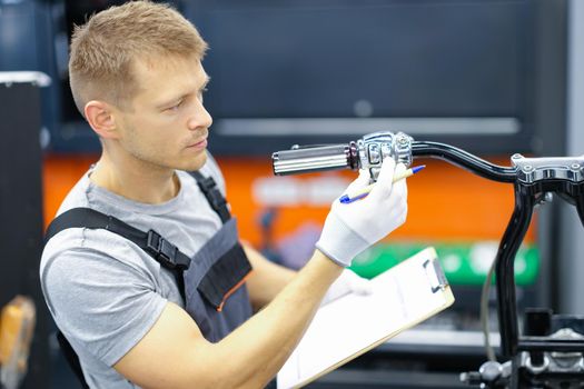 Young locksmith conducts diagnostics of motorcycle in service center. Motorcycle warranty service