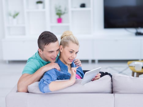 Young couple relaxing at luxurious home with tablet computers reading in the living room on the sofa couch.