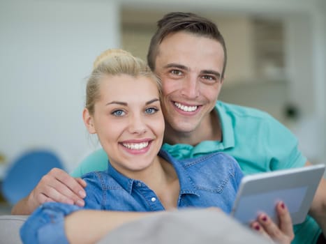 Young couple relaxing at luxurious home with tablet computers reading in the living room on the sofa couch.