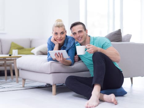 Young couple relaxing at luxurious home with tablet computers reading in the living room on the sofa couch.