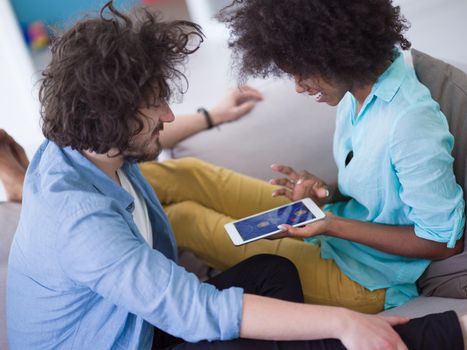 Young multiethnic couple sitting on a sofa in the luxury living room, using a tablet computer