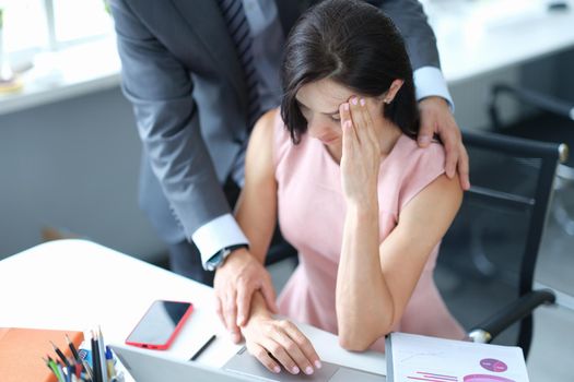 Businessman hugs embarrassed employee in office. Sexual harassment at work concept