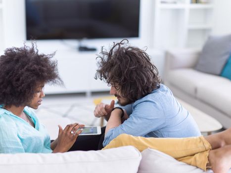 Young multiethnic couple sitting on a sofa in the luxury living room, using a tablet computer