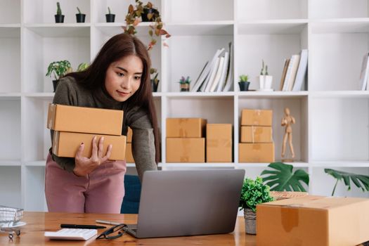 Start up small business entrepreneur SME or freelance asian woman using laptop with box, Young success Asian woman with her hand lift up , online marketing packaging box and delivery, SME concept