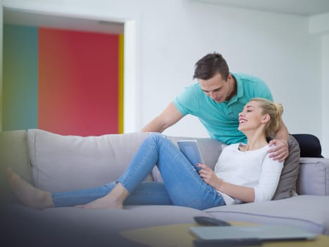 Young couple relaxing at luxurious home with tablet computers reading in the living room on the sofa couch.