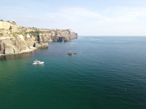 Sea landscape with rocky coastline on sunset time with cloudy sky. Yachts in the Sea on a background of rocky shores. The concept of perfect place for summer travel and rest.