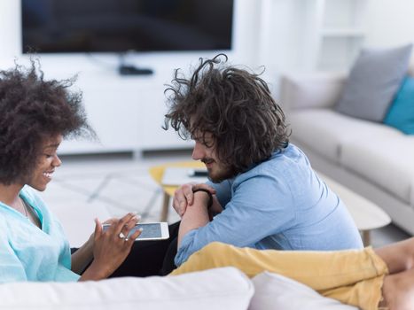 Young multiethnic couple sitting on a sofa in the luxury living room, using a tablet computer