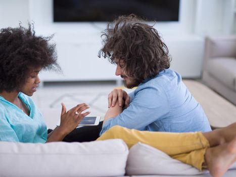 Young multiethnic couple sitting on a sofa in the luxury living room, using a tablet computer