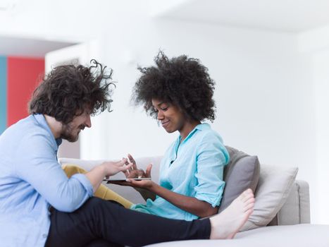 Young multiethnic couple sitting on a sofa in the luxury living room, using a tablet computer