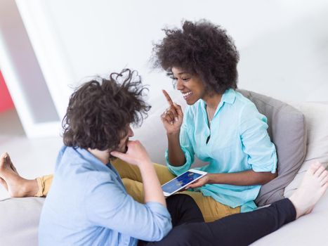 Young multiethnic couple sitting on a sofa in the luxury living room, using a tablet computer