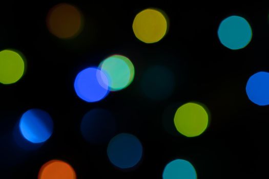 Defocused bokeh lights on black background, an abstract naturally blurred backdrop for Christmas eve or birthday party. Festive light texture. Colorful garland in blur. Overlay effect for design