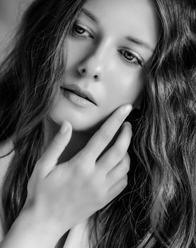 Beautiful woman applying cosmetics with her hand on face, natural look and wavy long hairstyle, beauty portrait and skincare routine concept