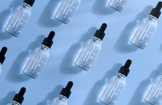 Pattern of transparent glass dropper bottle with air bubbles on blue background in sunlight. Pipette with fluid hyaluronic acid, serum, retinol. Cosmetics and healthcare concept. Luxury beauty product