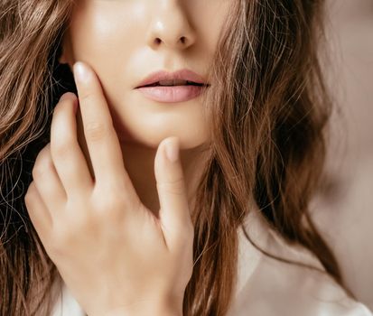 Beautiful woman applying cosmetics with her hand on face, natural look and wavy long hairstyle, beauty portrait and skincare routine concept