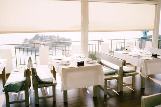 Restaurant with long benches and tables covered with tablecloths overlooking Sveti Stefan island . High quality photo