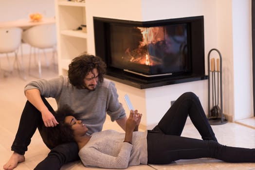 beautiful young multiethnic couple using tablet computer on the floor of their luxury home in front of fireplace at autumn day