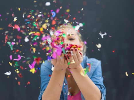 beautiful young woman celebrating new year and chrismas party while blowing confetti decorations to camera isolated over gray background