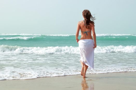 A beautiful girl is walking along the ocean shore. The concept of summer holidays