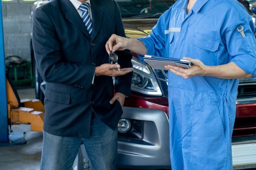 Close up shot automotive technician give car key back to customer after finish fix the problem of car in workplace area.