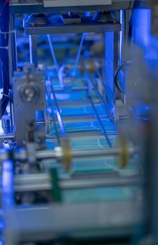 Part of conveyor belt of hygiene mask of the machine with blue light during work in the factory workplace.