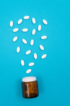 Global Pharmaceutical Industry and Medicinal Products - White Pills or Tablets Scattered from the Pill Container, Lying on Blue Background